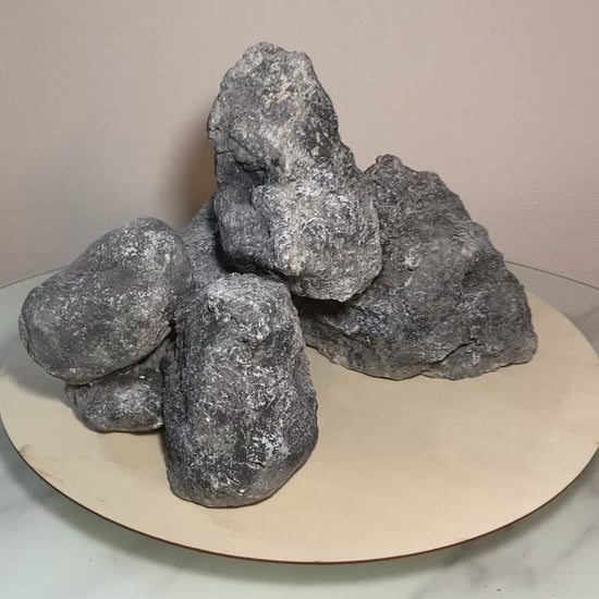 „Rotierendes Video einer grauen Aquarium-Höhlenformation aus drei verbundenen Felsen, präsentiert auf einem runden Tablett zur Ansicht der Höhleneingänge aus 360 Grad.“