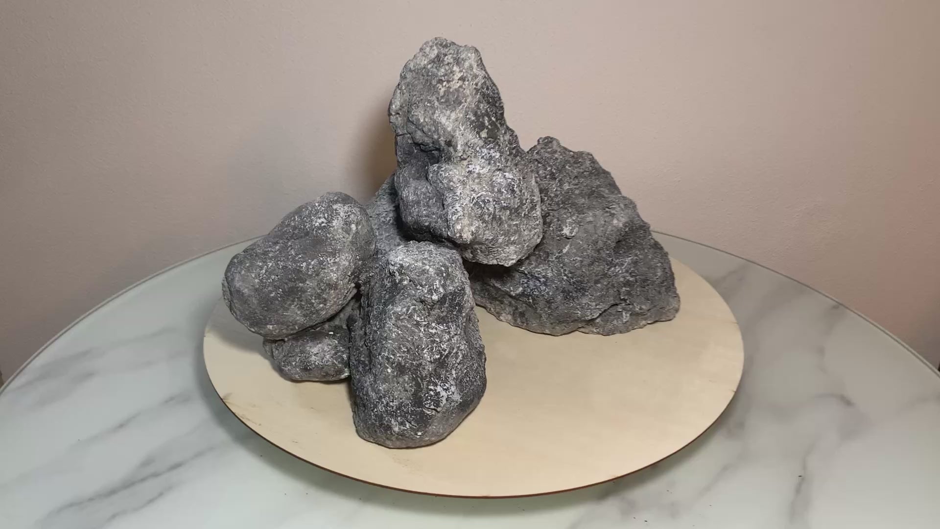 „Rotierendes Video einer grauen Aquarium-Höhlenformation aus drei verbundenen Felsen, präsentiert auf einem runden Tablett zur Ansicht der Höhleneingänge aus 360 Grad.“