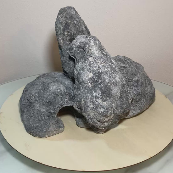 „Rotierendes Video einer grauen Aquarium-Höhlenformation aus drei verbundenen Felsen, präsentiert auf einem runden Tablett zur Ansicht der Höhleneingänge aus 360 Grad.“