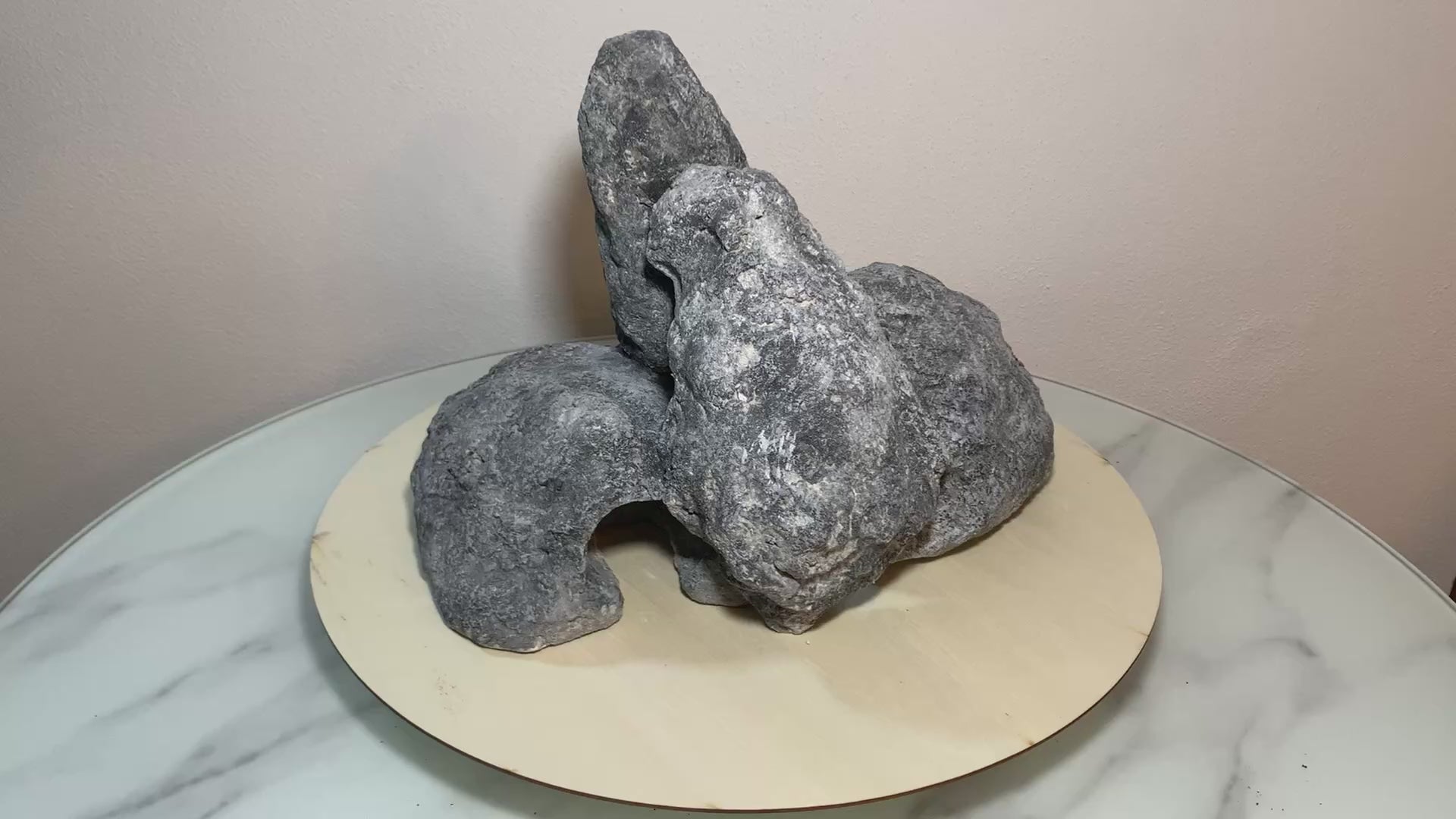 „Rotierendes Video einer grauen Aquarium-Höhlenformation aus drei verbundenen Felsen, präsentiert auf einem runden Tablett zur Ansicht der Höhleneingänge aus 360 Grad.“